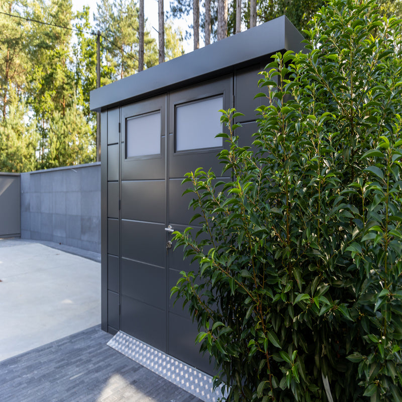 Telluria Sustainable Eleganto Steel Shed in Anthracite. Outside front right view of building in situ in a garden, showing pent roof and double opening front doors with windows. 9x8. Metal Ramp Accessory also shown.