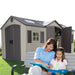 Lifetime 15x8 dual entrance plastic shed in beautiful cottage style. Front Left outside view with mother and daughter reading outside on a bench.